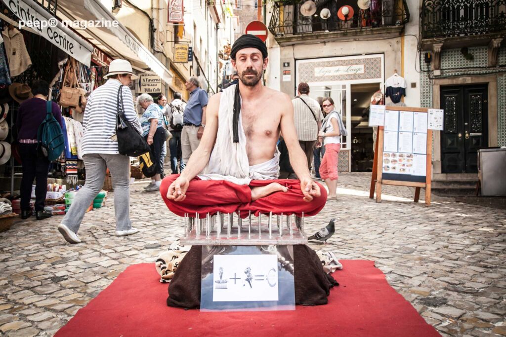 Street photography of Entertainer sitting on a bed of nails in Portugal by peep magazine / Photography by Cliff Sainsbury